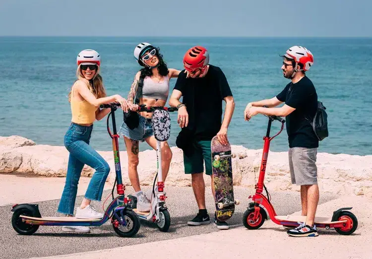 Group of men and women at the beach with Mii2 Stand 2.0 Electric Scooters in different colours.